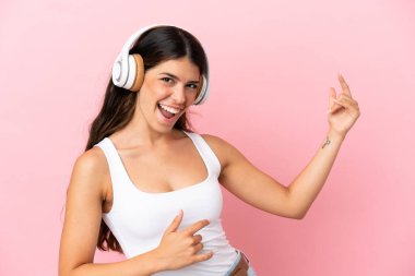 Genç beyaz kadın pembe arka planda izole edilmiş müzik dinliyor ve gitar hareketi yapıyor.