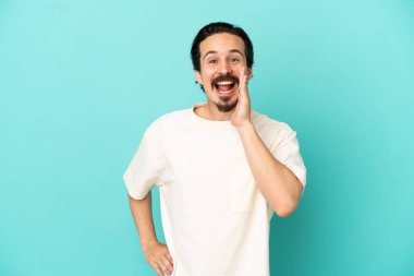 Mavi arka planda izole edilmiş genç beyaz adam ağzı açık bağırıyor.