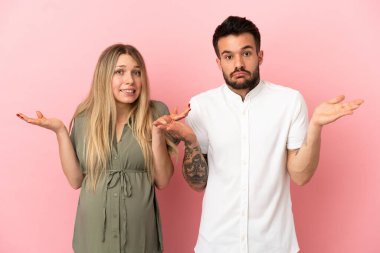 Hamile kadın ve erkek soyutlanmış pembe arka planda kuşkuları ve kafa karıştırıcı ifadeleri var.