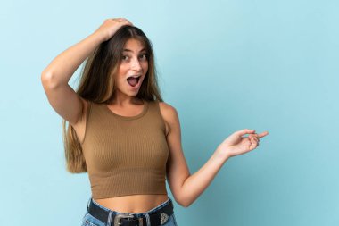 Mavi arka planda izole edilmiş genç beyaz kadın şaşırdı ve işaret etti.