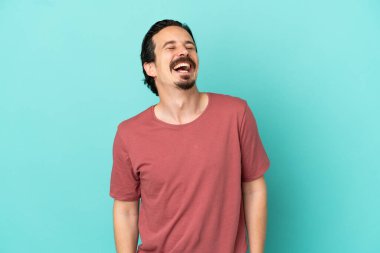 Kafkasyalı genç adam mavi arka planda tek başına gülüyor.