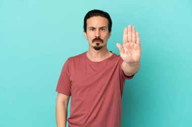 Mavi arka planda izole edilmiş genç beyaz adam dur hareketi yapıyor.