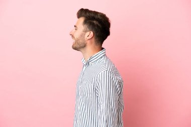 Beyaz tenli yakışıklı, pembe arka planda izole edilmiş. Yan pozisyonda gülüyor.