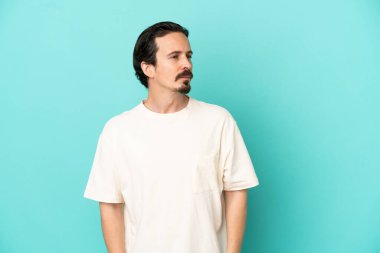 Mavi arka planda izole edilmiş genç beyaz adam yan tarafa bakıyor.