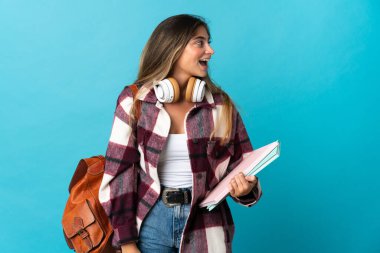 Genç bayan öğrenci mavi arka planda izole edilmiş. Yan pozisyonda gülüyor.