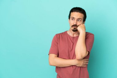 Kafkasyalı genç adam mavi arka planda izole edilmiş, yorgun ve sıkılmış bir ifadeyle