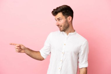 Pembe arka planda izole edilmiş beyaz tenli yakışıklı bir adam, parmağını yana uzattı ve bir ürün sundu.