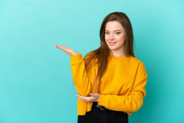 İzole edilmiş mavi arka planda genç bir kız. Davet etmek için ellerini yana uzatıyor.