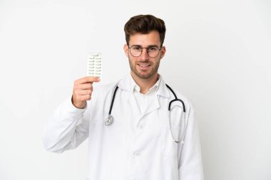Beyaz arka planda izole edilmiş beyaz bir doktor doktor önlüğü giyiyor ve elinde haplar var.