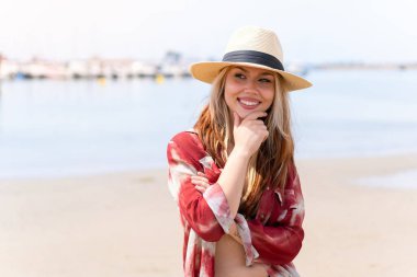 Yaz tatilinde genç ve güzel bir kadın sahilde yan tarafa bakıyor.