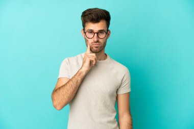 Beyaz tenli yakışıklı bir adam mavi arka planda izole edilmiş ve düşünüyor.