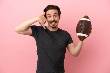 Pembe arka planda ragbi oynayan beyaz bir adam telefon jesti yapıyor. Bana geri dönüş işareti ver.