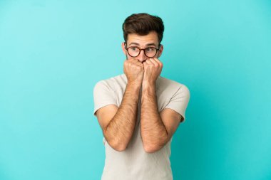 Genç, beyaz, yakışıklı bir adam mavi arka planda izole edilmiş. Gergin ve korkmuş.