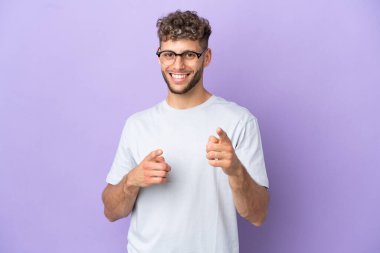 Mor arka planda izole edilmiş beyaz adam şaşırmış ve ön tarafı işaret ediyor.