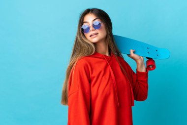 Kafkasyalı genç bir kadın mavi arka planda izole edilmiş mutlu bir ifadeyle paten kayıyor.