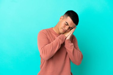 Soyutlanmış mavi arka planda genç yakışıklı bir adam uyku jesti yapıyor.