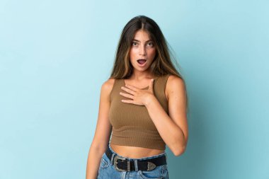 Mavi arka planda izole edilmiş genç beyaz kadın sağa bakarken şaşırdı ve şok oldu.