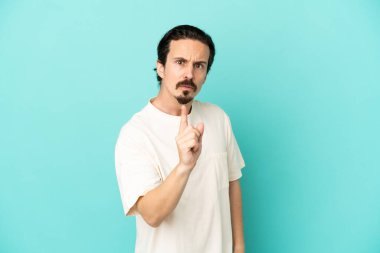 Mavi arka planda izole edilmiş genç beyaz adam hayal kırıklığına uğramış ve ön tarafı işaret ediyor.