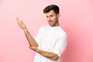Pembe arka planda soyutlanmış beyaz tenli yakışıklı adam davet edildiği için ellerini yana uzatıyor.