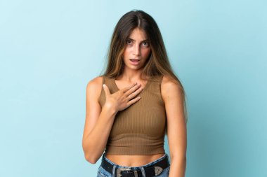 Mavi arka planda izole edilmiş genç beyaz kadın kendini işaret ediyor.