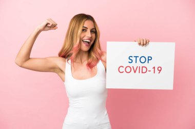 Pembe arka planı olan genç bir kadın elinde yazılı bir pankartla Covid 19 'u durdur ve güçlü bir hareket yap.