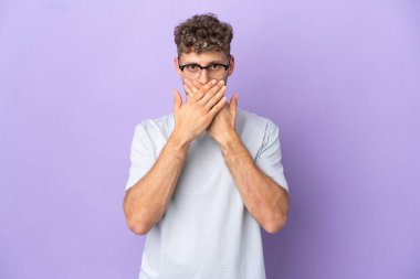 Teslimatçı beyaz adam mor arka planda izole edilmiş ağzı elleriyle kapatıyor.