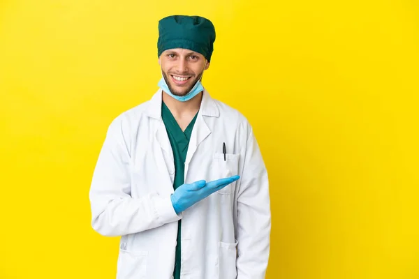 Χειρουργός Ξανθός Άνδρας Πράσινη Στολή Απομονωμένος Κίτρινο Φόντο Παρουσιάζοντας Μια — Φωτογραφία Αρχείου