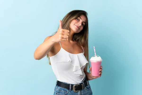 Ung Kvinna Med Jordgubbsmjölkshake Isolerad Blå Bakgrund Med Tummen Upp — Stockfoto