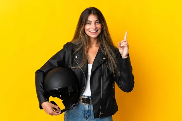 黄色の背景に隔離されたオートバイのヘルメットを保持し 最高の兆候で指を持ち上げる女性 — ストック写真
