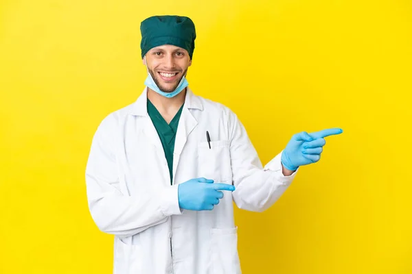 Χειρούργος Ξανθός Άνδρας Πράσινη Στολή Απομονωμένος Κίτρινο Φόντο Δείχνοντας Δάχτυλο — Φωτογραφία Αρχείου