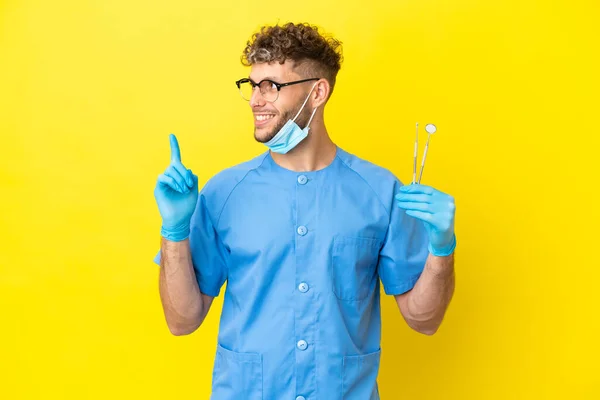 Dentysta Blondynka Mężczyzna Trzyma Narzędzia Izolowane Tle Wskazując Świetny Pomysł — Zdjęcie stockowe