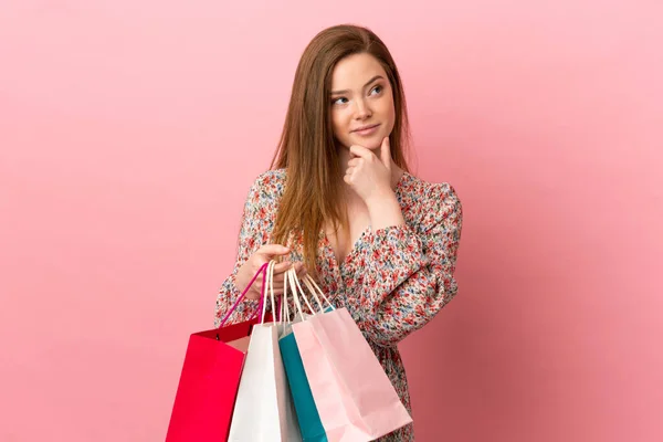 Tiener Meisje Geïsoleerde Roze Achtergrond Holding Boodschappentassen Denken — Stockfoto