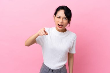 Pembe arka planda izole edilmiş genç Vietnamlı kadın hayal kırıklığına uğramış ve ön tarafı işaret ediyor.