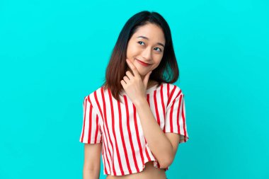 Genç Vietnamlı kadın mavi arka planda izole edilmiş mutlu ve gülümsüyor.