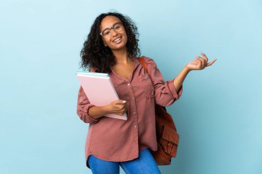 Mavi arka planda izole edilmiş genç bir kız. Davet edilmek için ellerini yana uzatıyor.