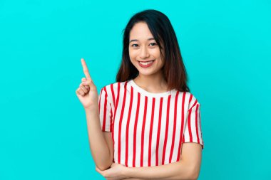 Genç Vietnamlı kadın mavi arka planda izole edilmiş mutlu ve yukarıya bakıyor.