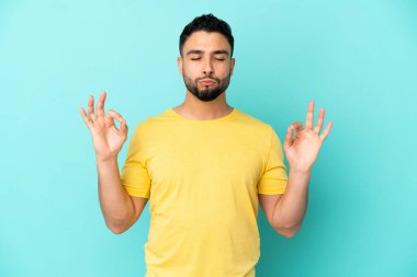 Genç Arap adam Zen pozunda mavi arka planda izole edilmiş.