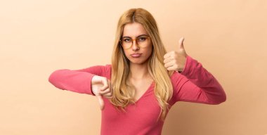 Genç Uruguaylı sarışın kadın izole edilmiş bir şekilde iyiye-kötüye işaret veriyor. Evet ya da hayır arasında kararsız