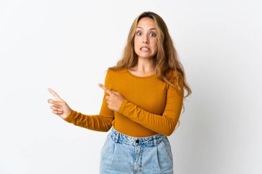 Mavi arka planda izole edilmiş genç sarışın kadın korkmuş ve kenarı işaret ediyor.