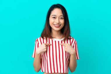 Genç Vietnamlı kadın, mavi arka planda izole edilmiş, şaşırmış bir yüz ifadesi var.