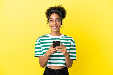 Genç Afrikalı Amerikalı kadın sarı arka planda izole edilmiş kameraya bakıyor ve gülümsüyor.