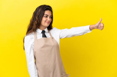 Kafkas restoranındaki genç garson sarı arka planda izole edilmiş bir şekilde baş parmak hareketi yapıyor.