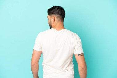 Genç Arap adam arka planda mavi arka planda izole edilmiş ve yana bakıyor.