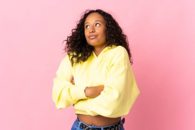 Kübalı genç bir kız pembe arka planda izole edilmiş. Omuzlarını kaldırırken şüpheli hareketler yapıyor.