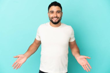 Genç Arap adam mavi arka planda izole edilmiş mutlu ve gülümsüyor