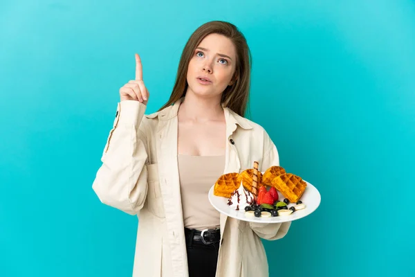 Adolescente Menina Segurando Waffles Sobre Isolado Fundo Azul Pensando Uma — Fotografia de Stock