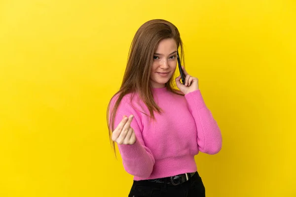 ティーン少女使用携帯電話上の隔離された黄色の背景作るお金ジェスチャー — ストック写真