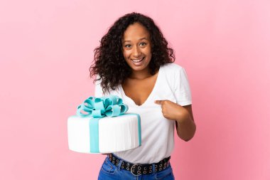 Pasta şefi elinde büyük bir pasta tutuyor. Pembe arka planda ve yüzünde sürpriz bir ifade var.