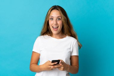 Mavi arka planda izole edilmiş genç sarışın kadın şaşırdı ve bir mesaj gönderiyor.