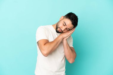 Genç Arap adam mavi arka planda izole edilmiş bir şekilde uyku jesti yapıyor.